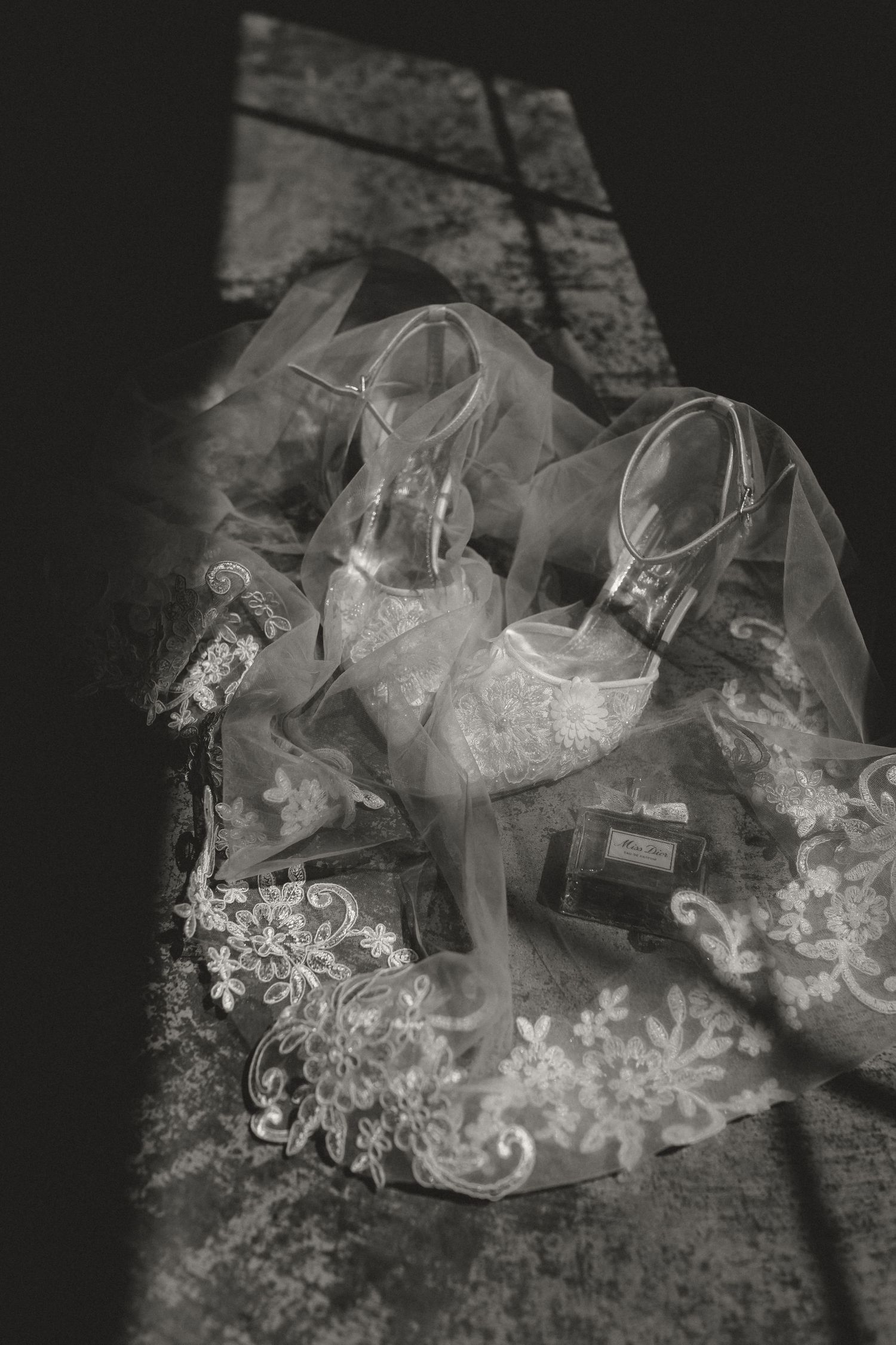 Elegant white lace wedding shoes arranged with delicate veil in dramatic lighting.