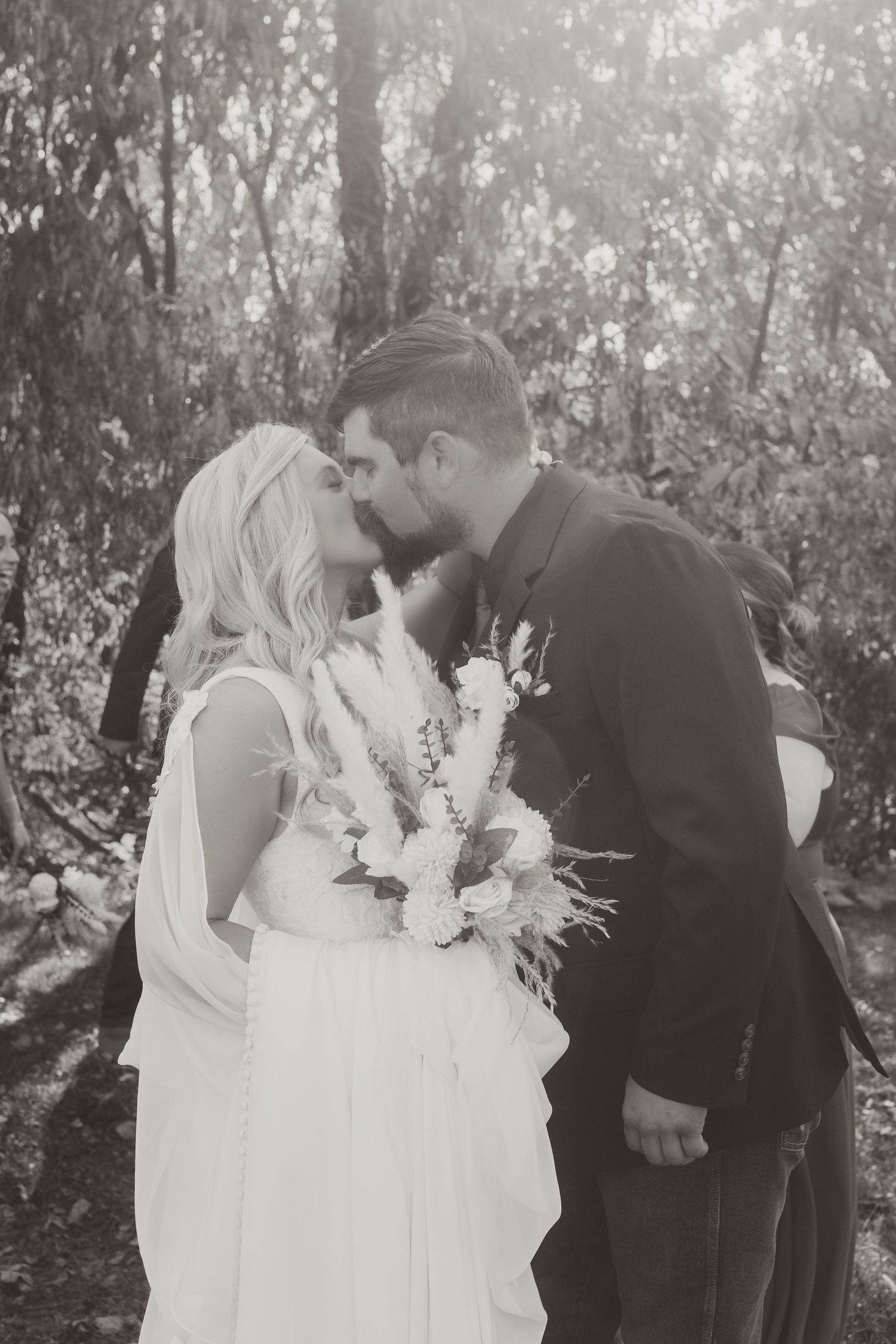 Tender wedding moment captured in black and white as newlyweds kiss holding white floral bouquet.