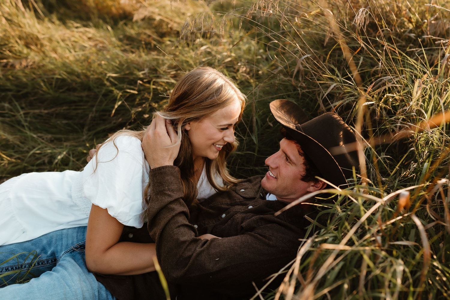 A romantic couple lying in tall golden grass during sunset.