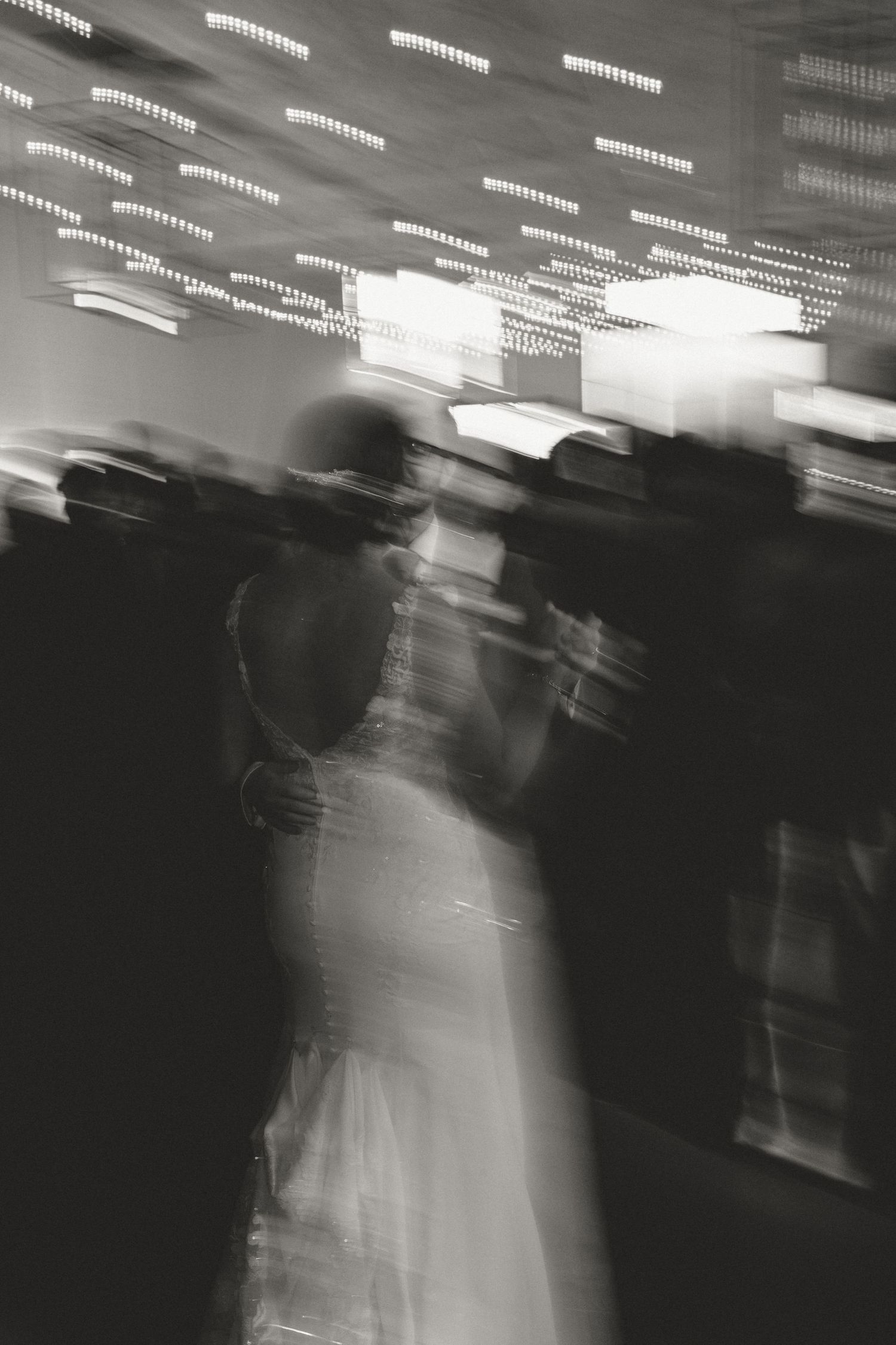 Abstract black and white motion blur of dancers at a reception with overhead lights.