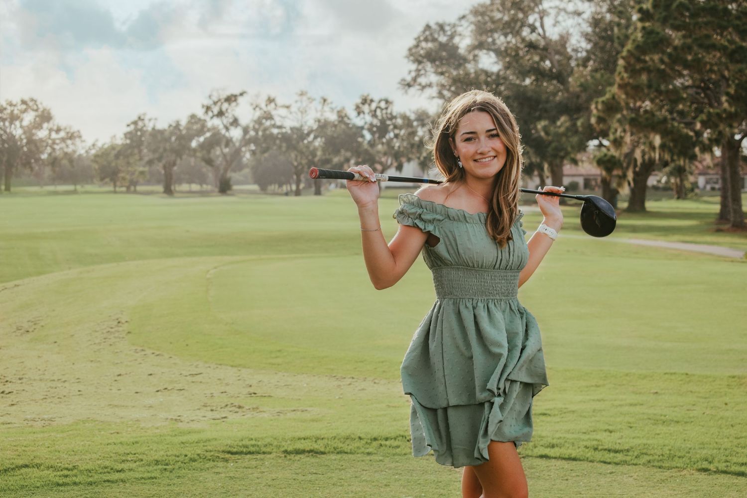 Senior girl posing confidently with golf club on green course.