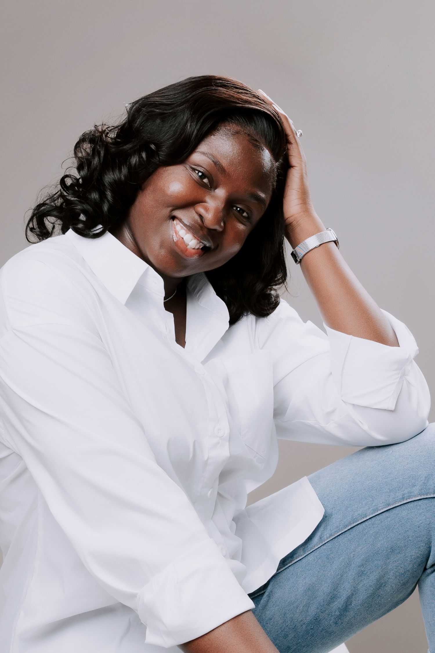 A smiling woman wearing a white shirt and blue jeans shot against a neutral background, perfect for professional headshots in Basildon Essex