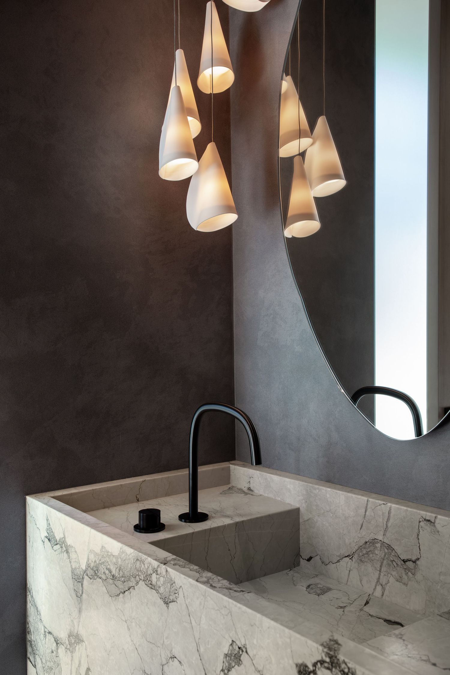 Modern bathroom design featuring cone pendant lights above a marble vanity with matte black faucet and circular mirror.