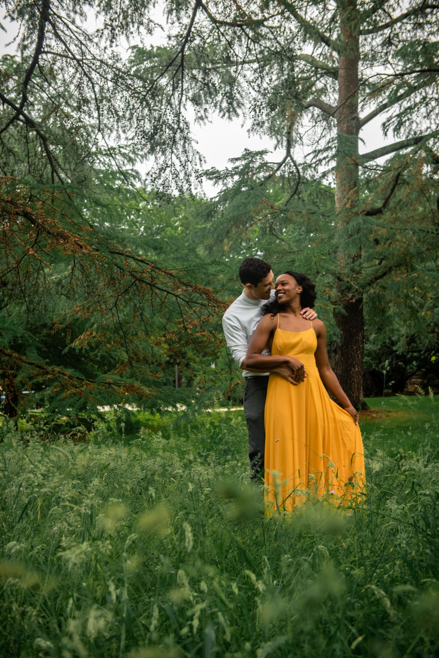 A couple shares an intimate moment in a lush forest setting, with the woman wearing a vibrant yellow dress.