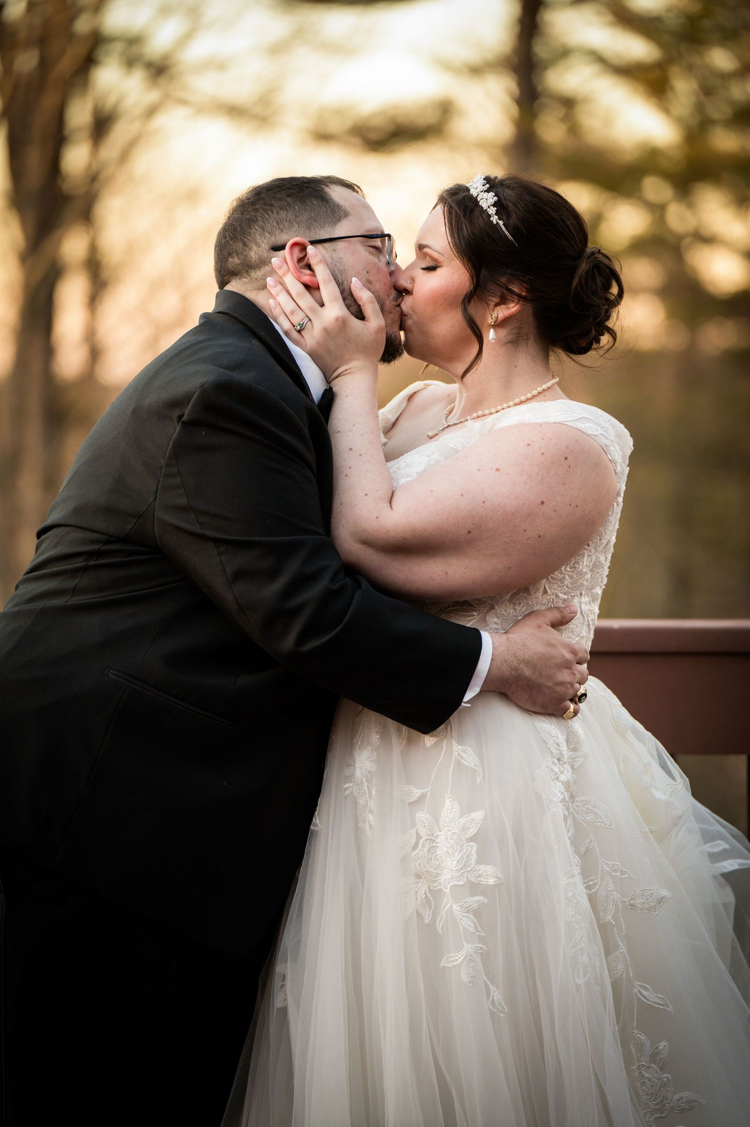 A romantic wedding kiss captured at sunset with the bride in a flowing white lace gown and groom in classic black tuxedo.