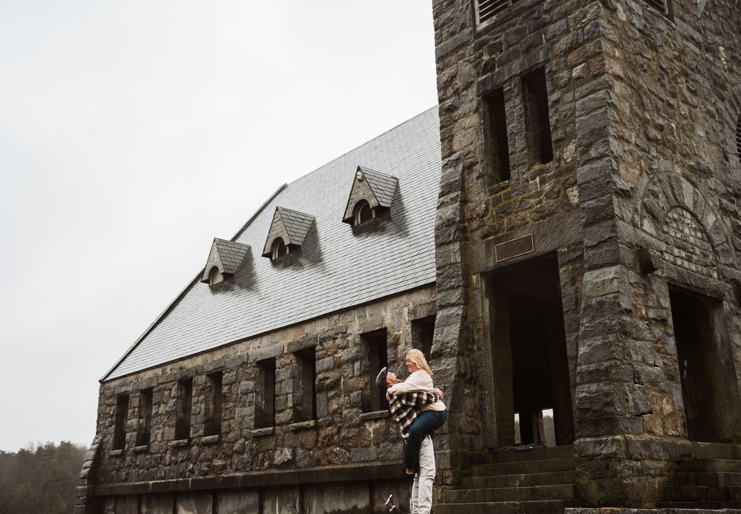 A figure stands outside a stone castle-like building with snow covered dormers on an overcast winter day.