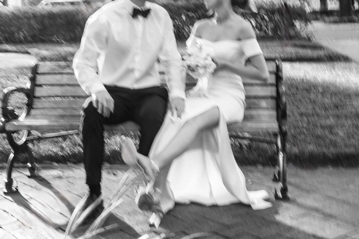A black and white photograph showing people in wedding attire jumping on a trampoline in an outdoor setting.