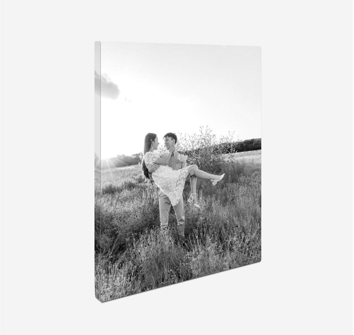A black and white artistic photograph of two people embraced in a romantic pose in a grassy meadow.