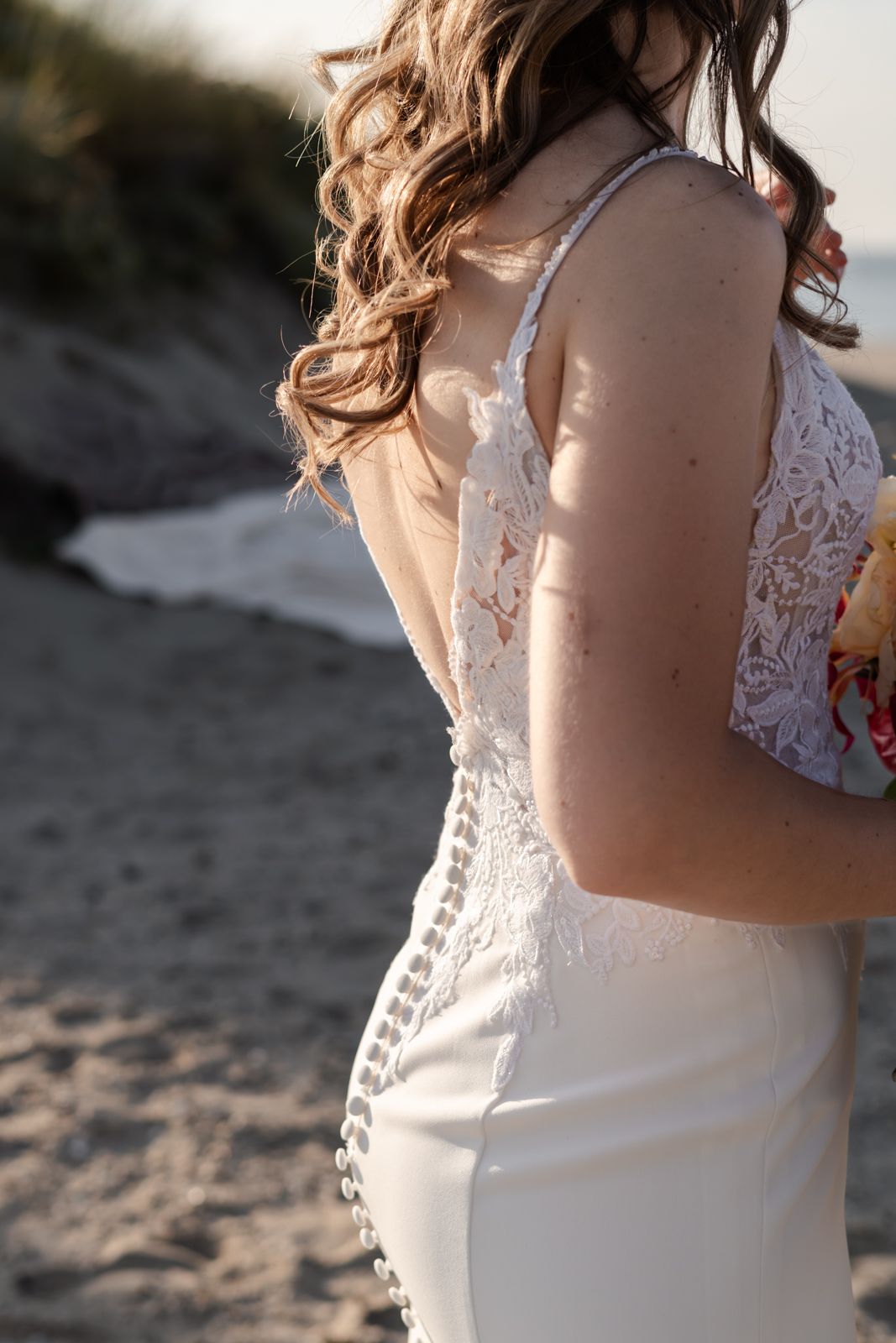 Close-up detail of lace wedding dress buttons and fabric in natural light.