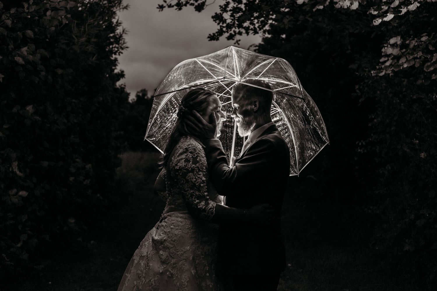 Wedding couple under illuminated transparent umbrella at night.