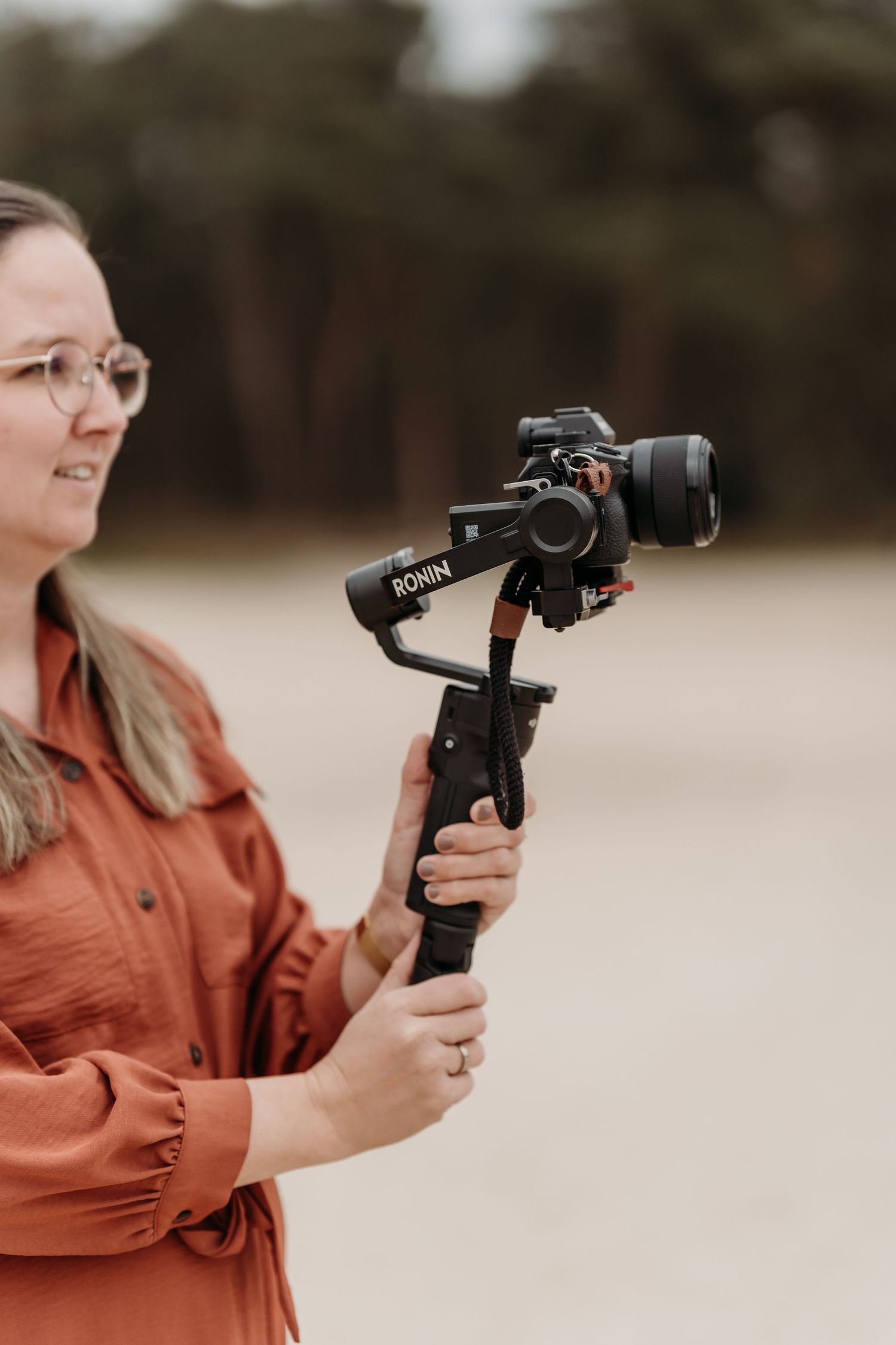 Photographer using a professional camera gimbal stabilizer while wearing a rust-colored shirt outdoors.