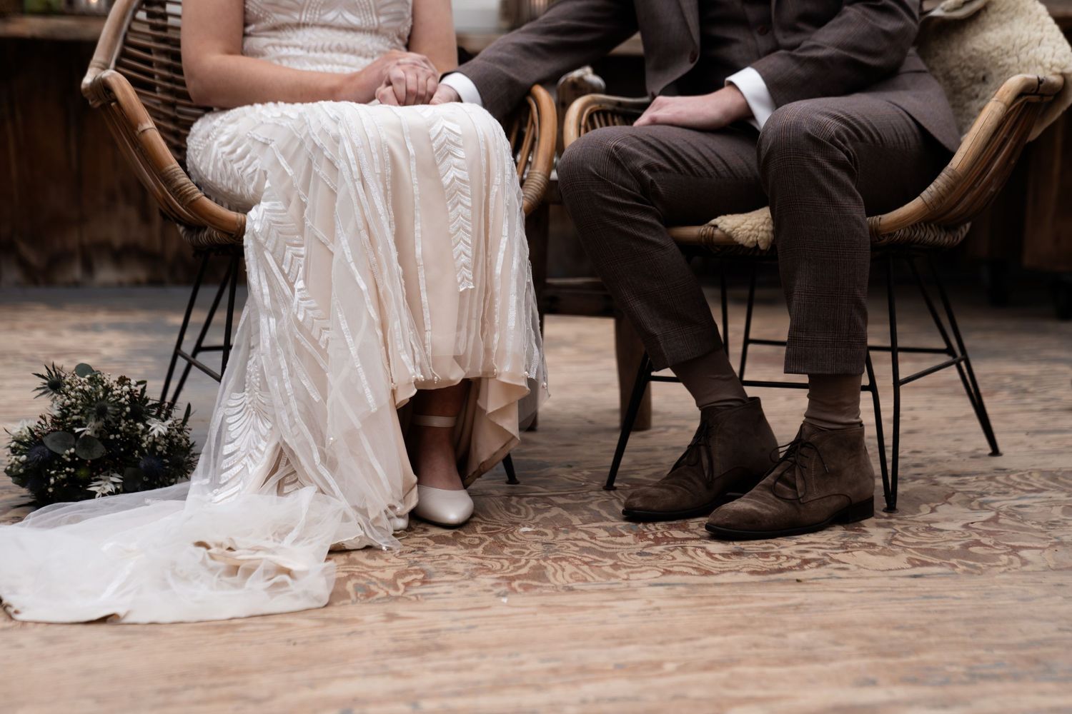 Elegant close-up of wedding attire showing white lace dress and brown leather boots on wooden floor.