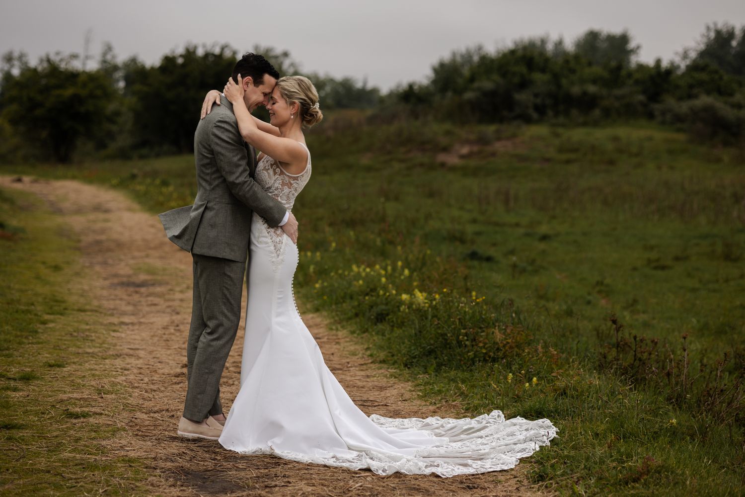 Intimate embrace between newlyweds on rural path with flowing white dress.