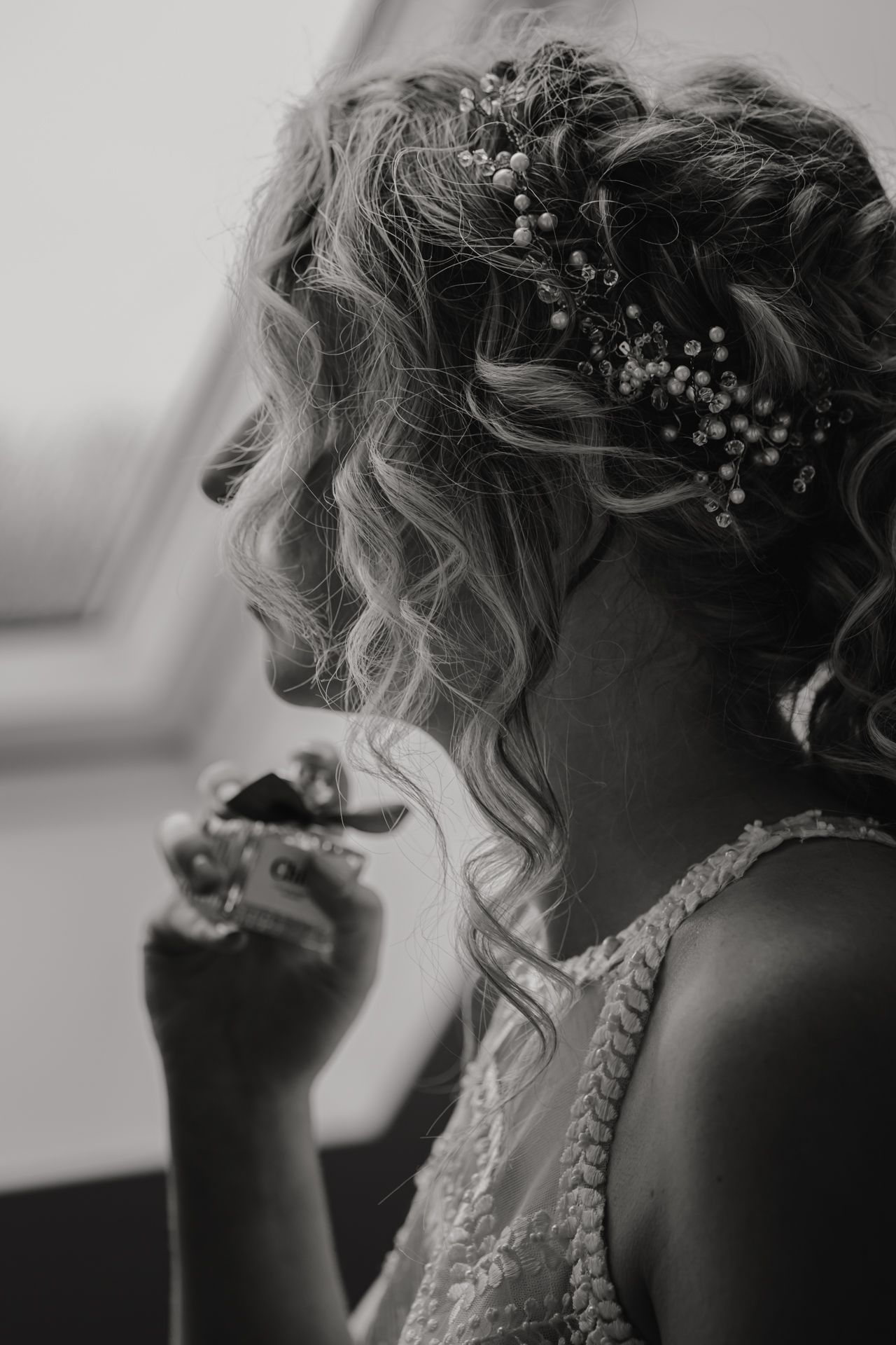 Black and white portrait photograph showing curled hair adorned with small flowers and a delicate white lace dress.