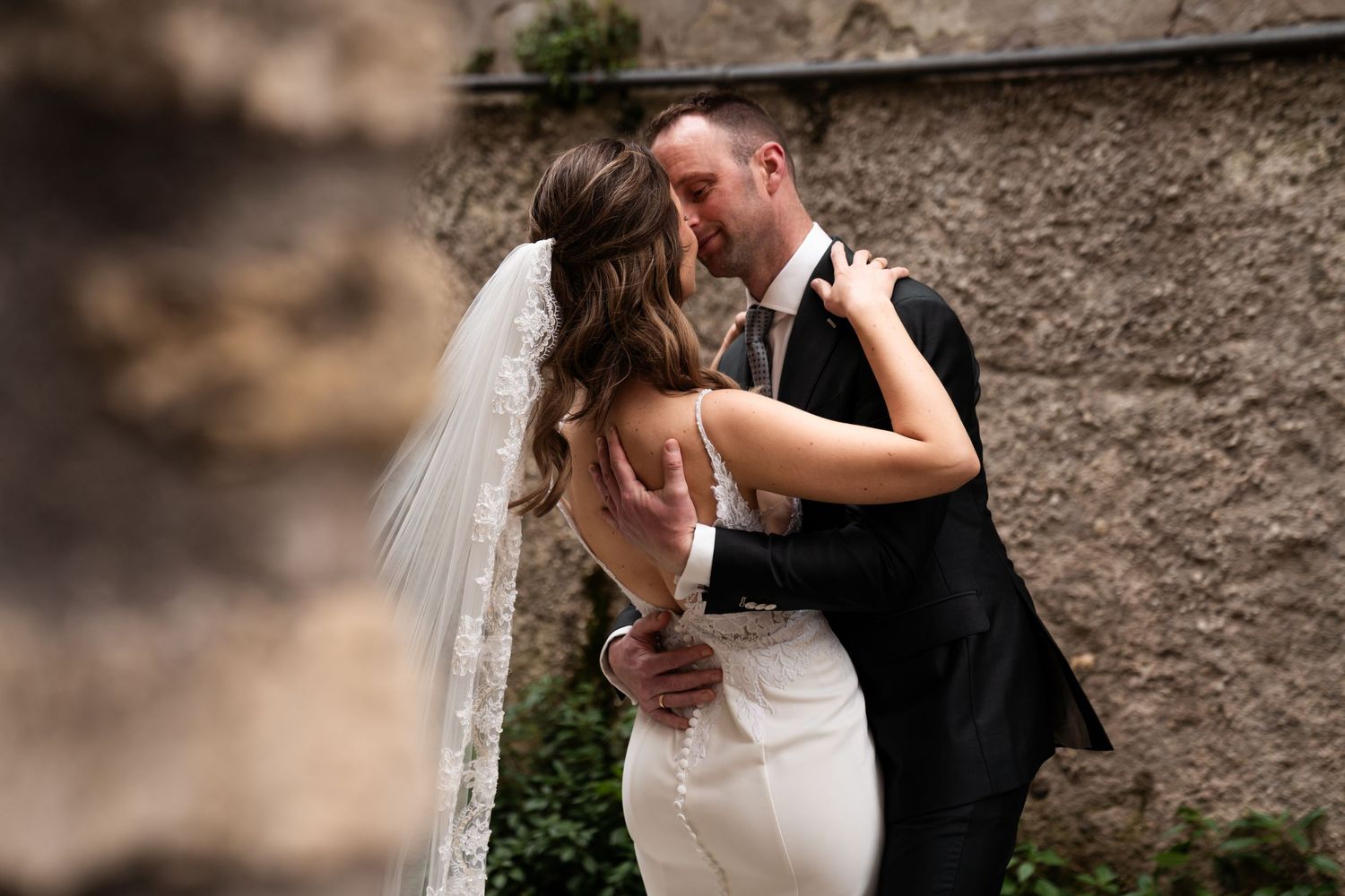 Romantic moment between newlyweds sharing a kiss against a stone wall on their wedding day.