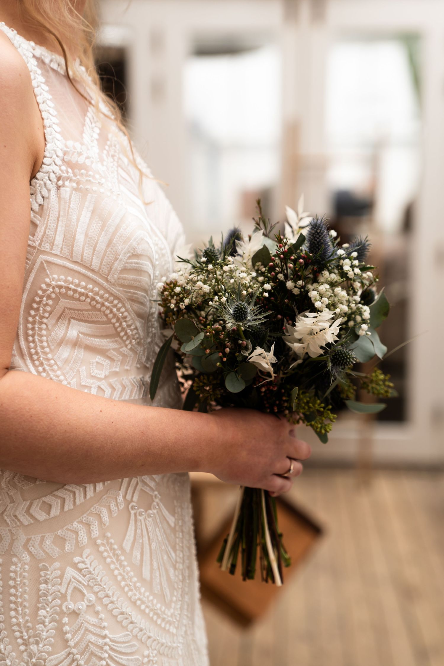 Close-up of white lace wedding dress detail and rustic bouquet.