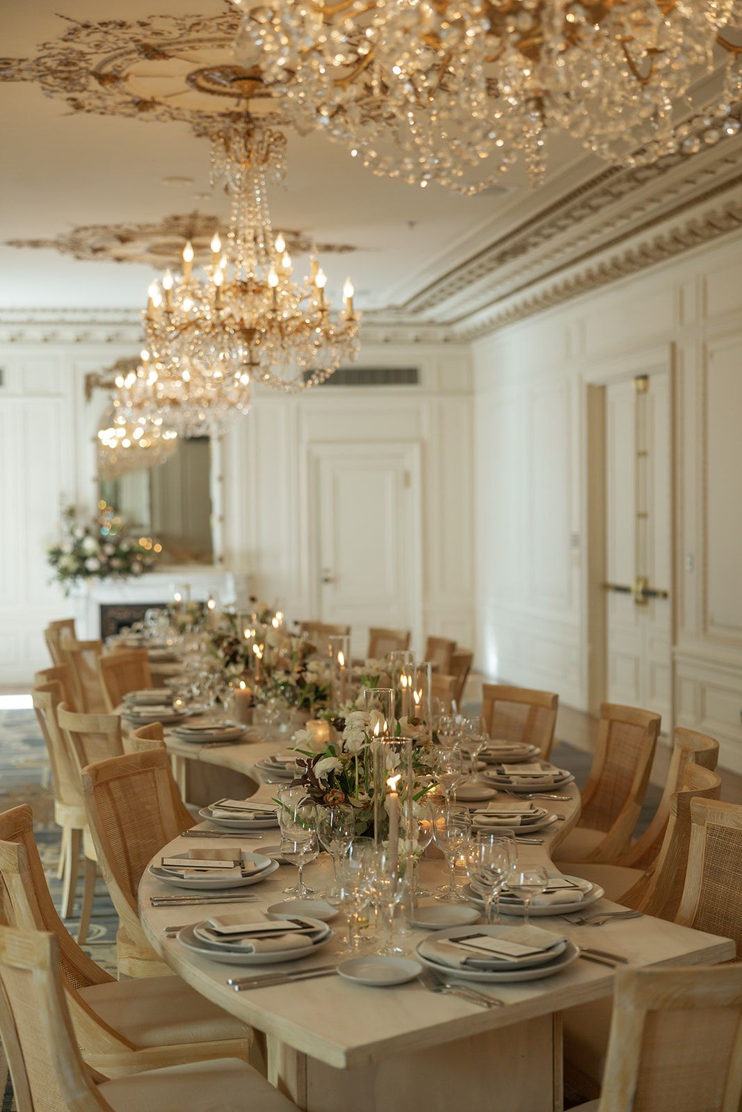 Elegant dining room with crystal chandeliers and table set for formal dinner with white linens and wooden chairs.