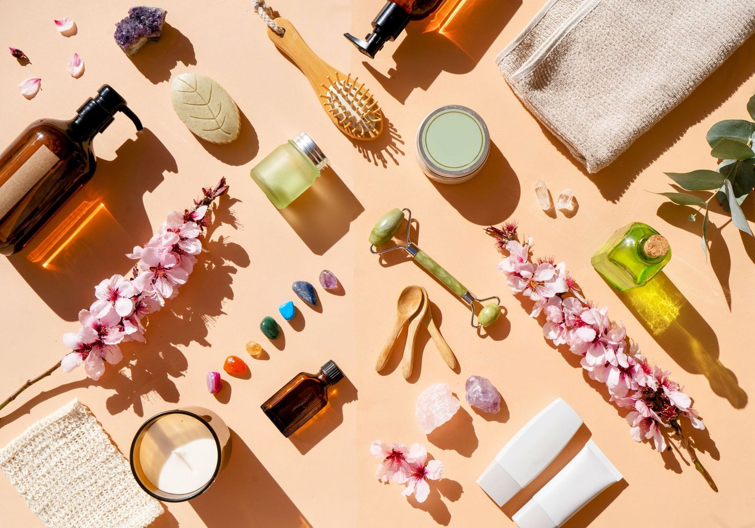 Flatlay of spa and wellness products with flowers, oils, and beauty items on peach background.