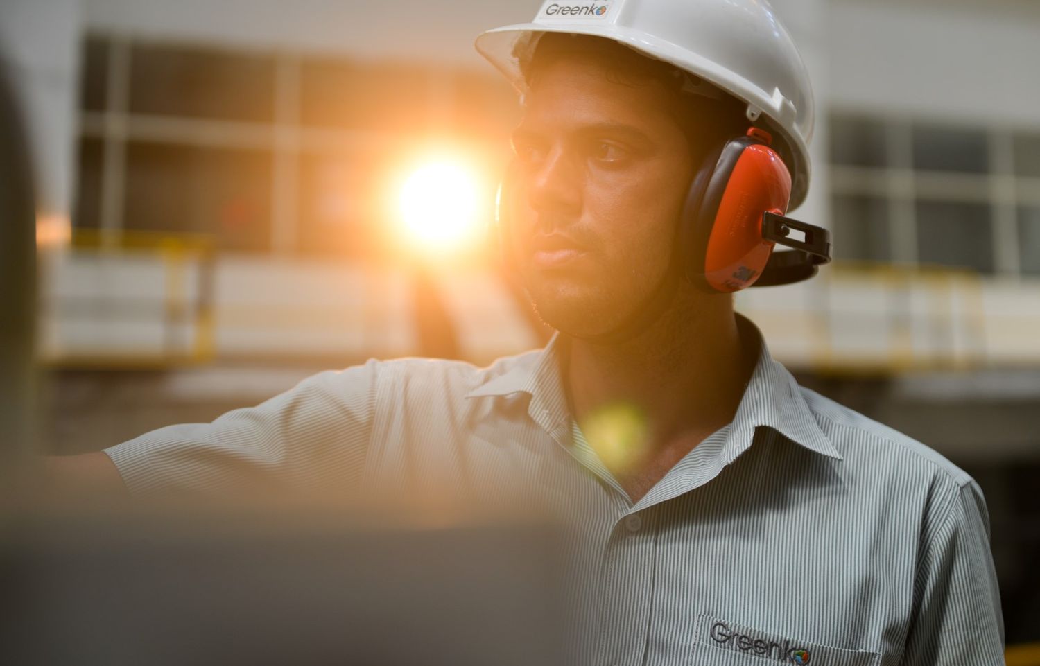 Industrial worker wearing protective gear and headphones in sunset lighting.
