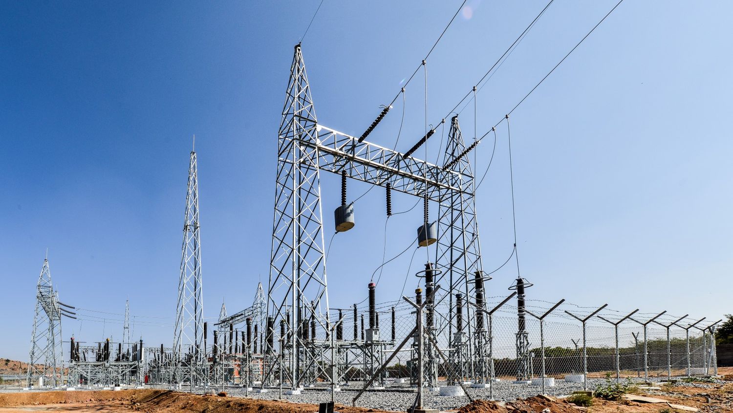 Electrical power substation with transmission towers and equipment against blue sky.