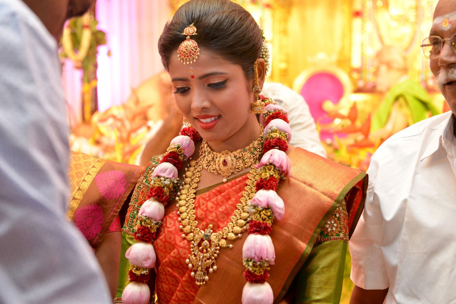Traditional South Indian bride wearing elaborate gold jewelry and red silk saree during ceremony.