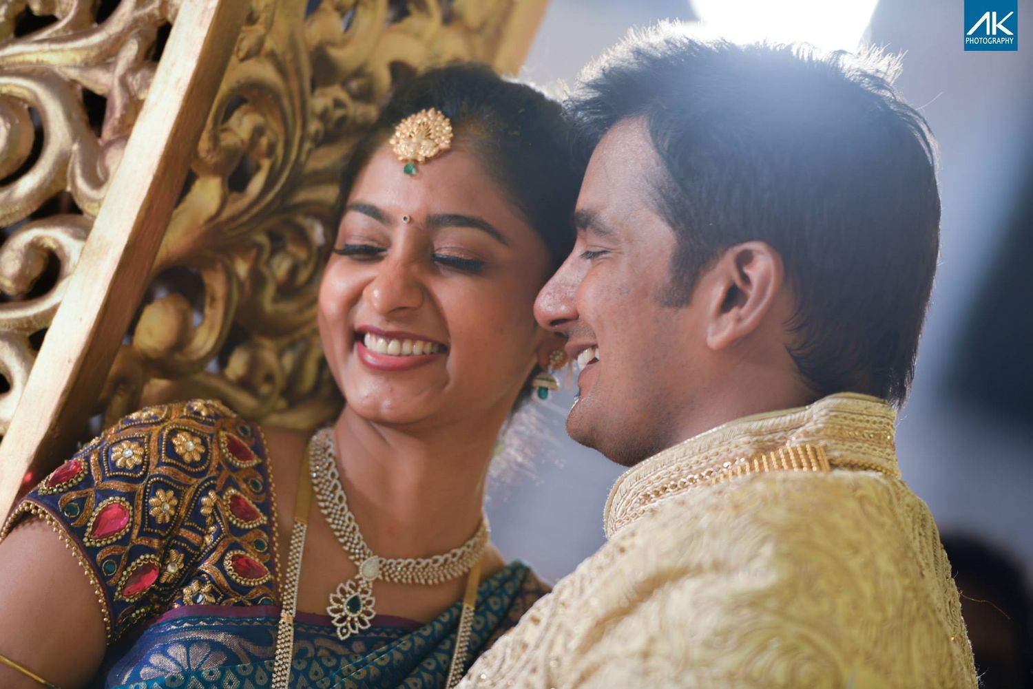 Couple in traditional Indian wedding attire sharing a joyful moment against decorative backdrop.