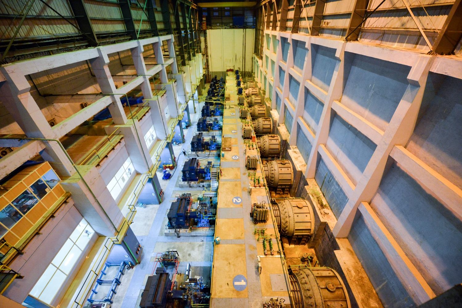 Interior of a power plant showing symmetrical rows of heavy machinery and equipment on multiple levels.