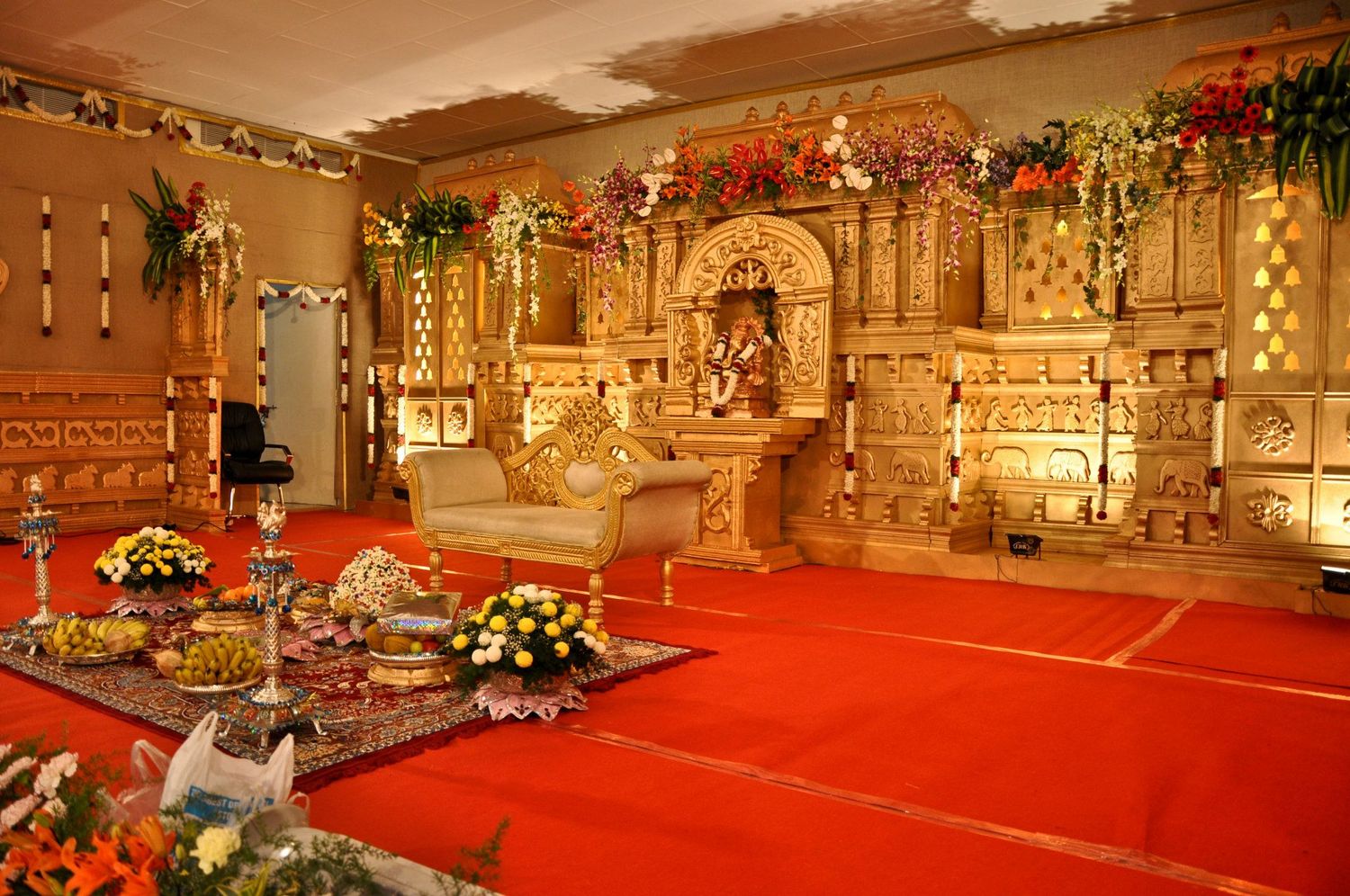 Ornate temple altar decorated with golden structures and floral arrangements on red carpet.