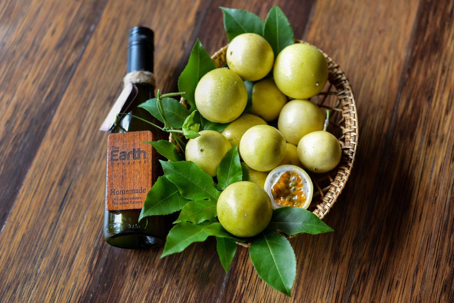 Fresh passion fruits and green leaves arranged in a basket with a wine bottle on wooden surface.