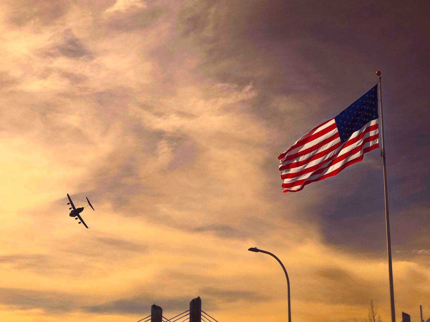 American flag waving against sunset sky with airplane silhouette passing by.