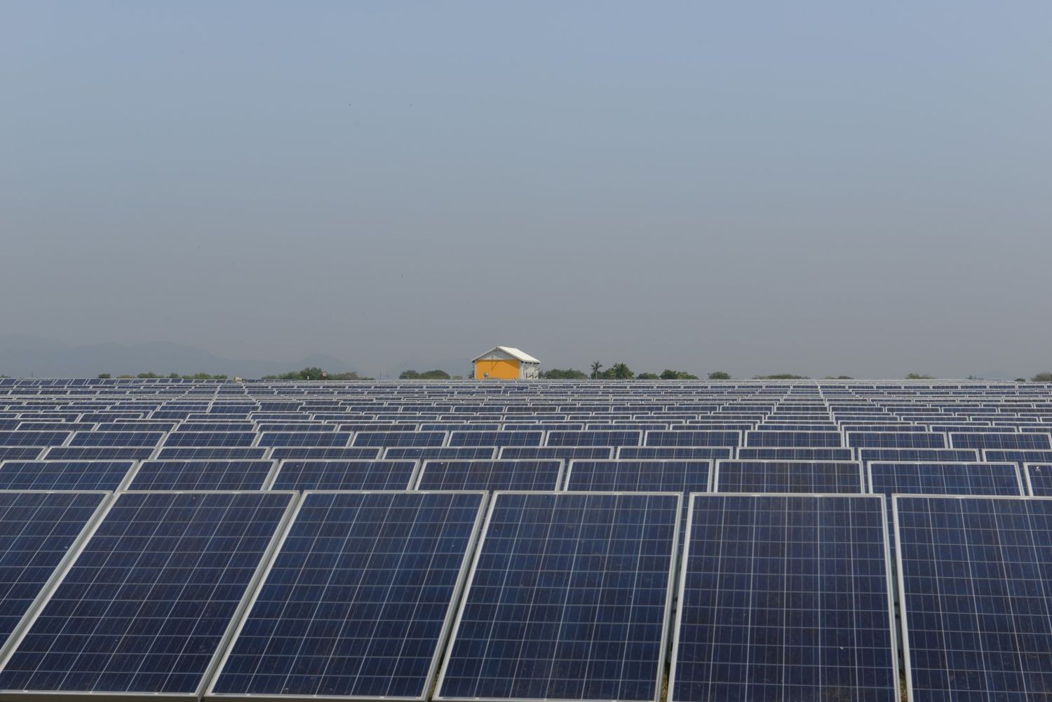 Large-scale solar power installation with rows of panels and a small yellow building in the distance.