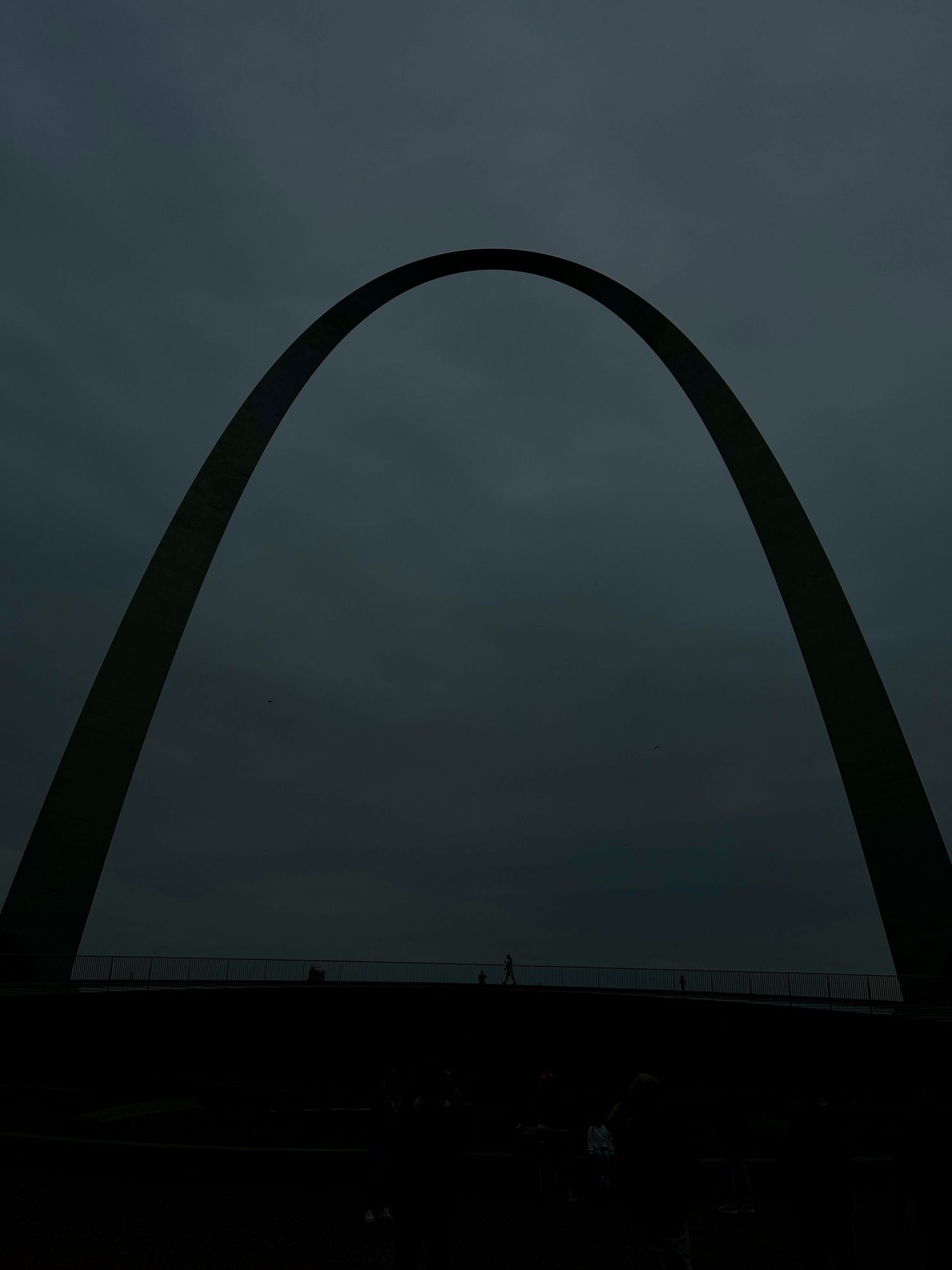 Dramatic silhouette of the Gateway Arch against dark stormy skies at dusk.