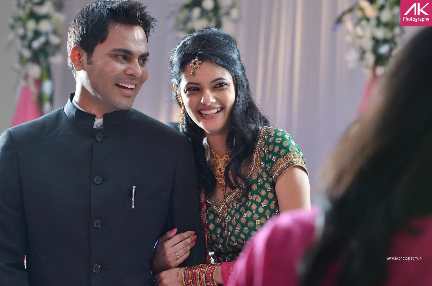 Couple in traditional Indian attire at wedding celebration with floral decorations.