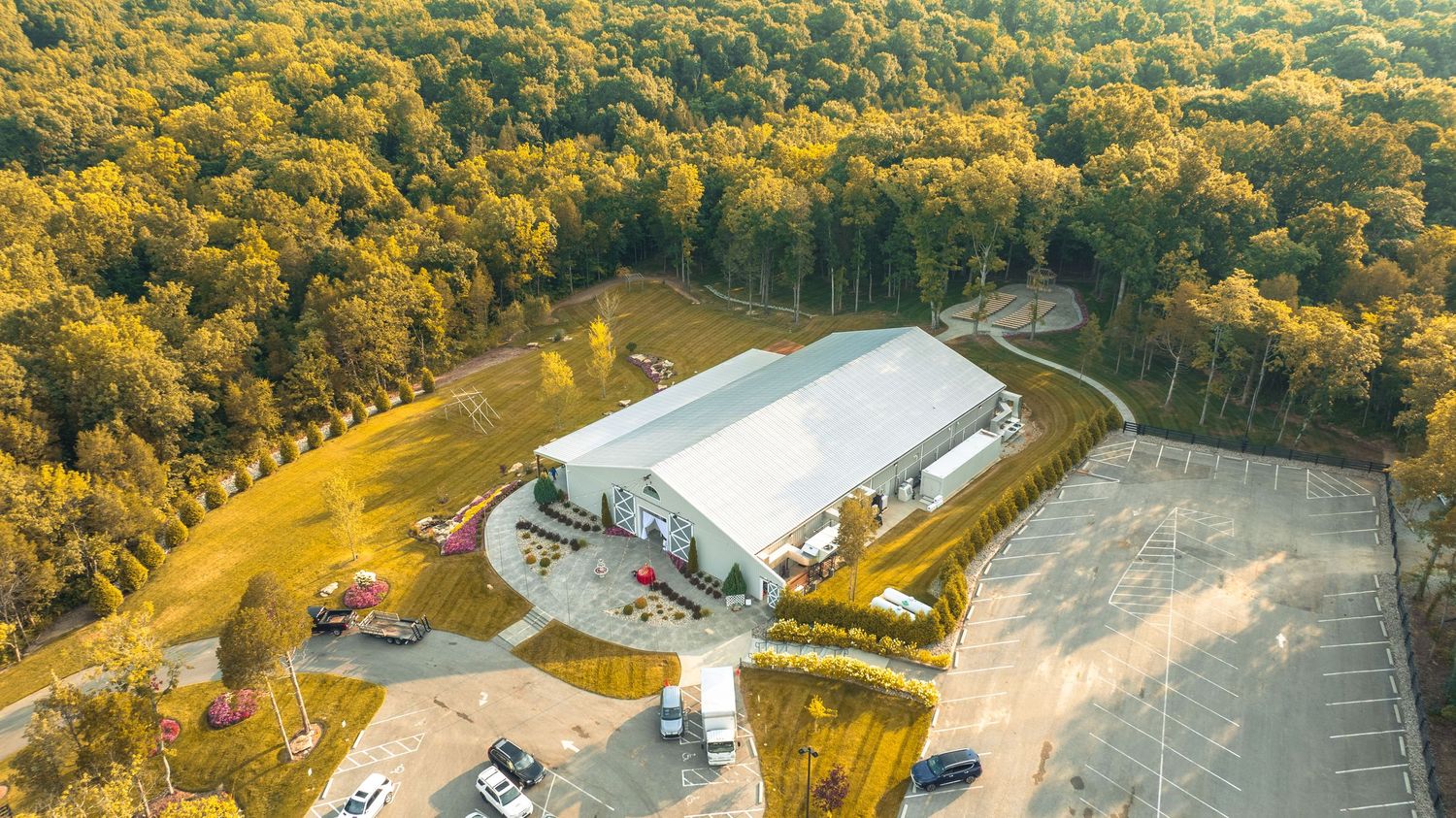 Aerial view of a large industrial warehouse building surrounded by autumn forest and parking area.