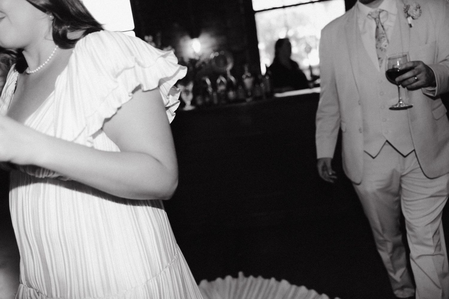 A candid black and white shot of guests at a wedding reception with someone in a white dress.