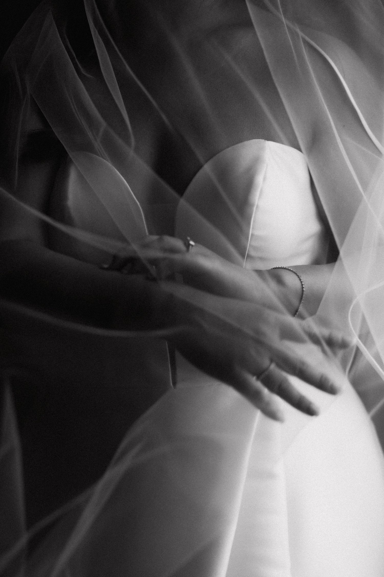 Close-up of delicate white fabric draped over a wedding dress with hands gently touching the material.