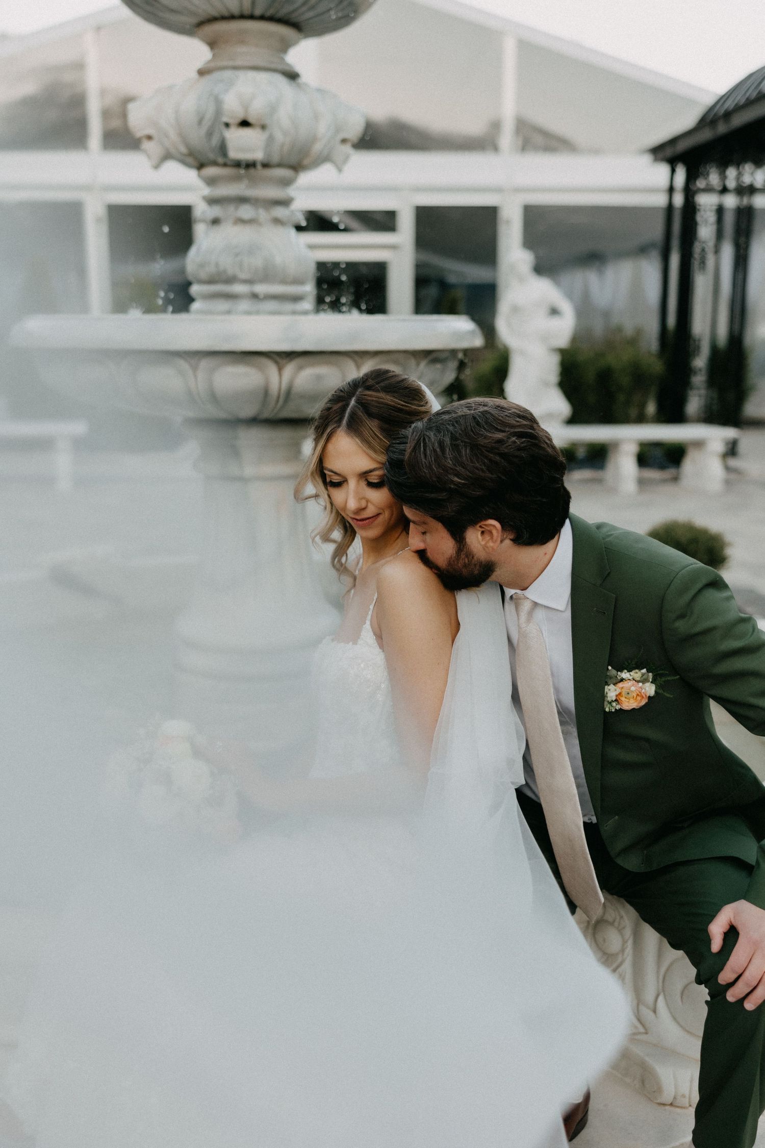 A romantic wedding moment by an ornate fountain with the couple in elegant attire.
