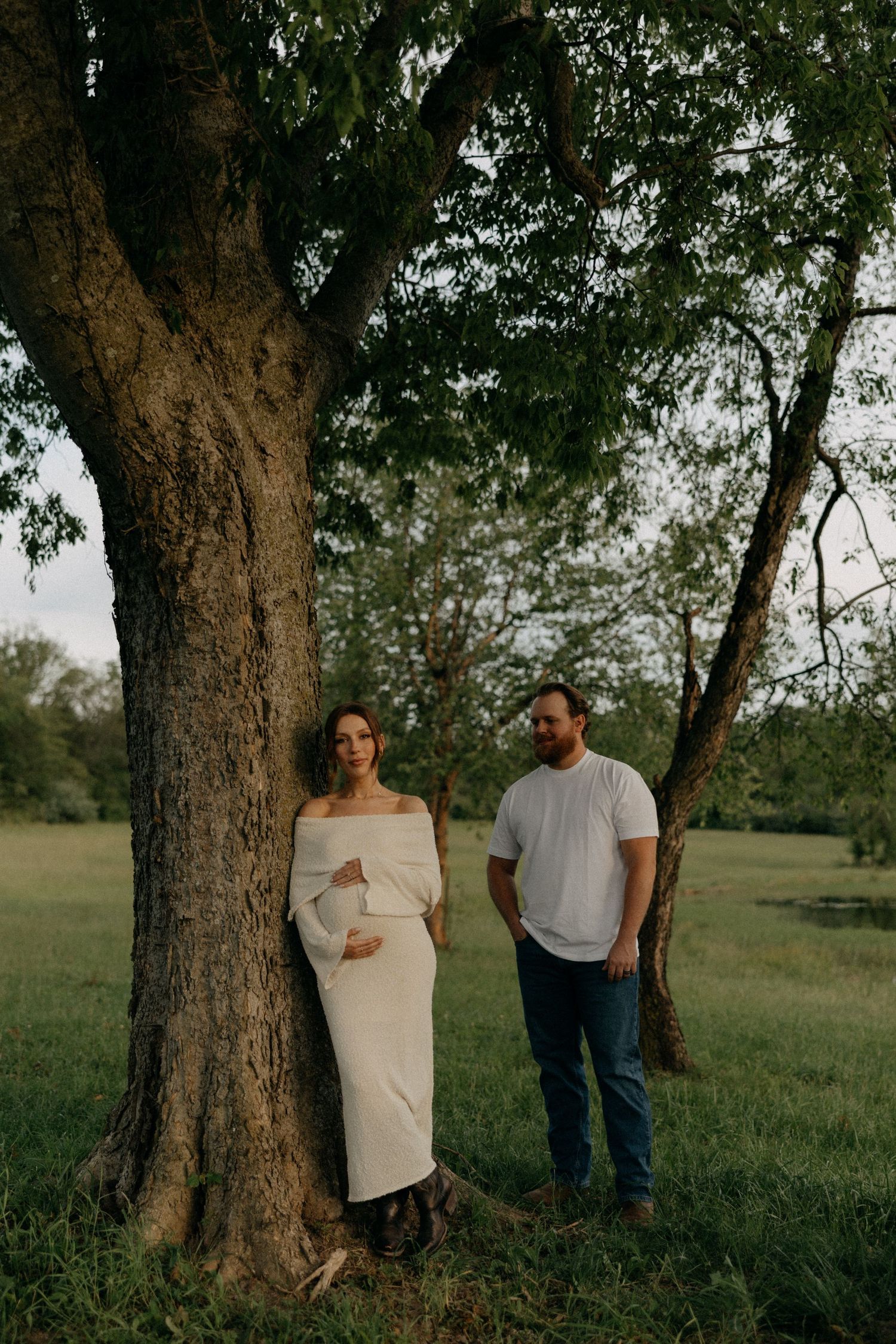 Maternity photo session near large trees in natural outdoor setting.
