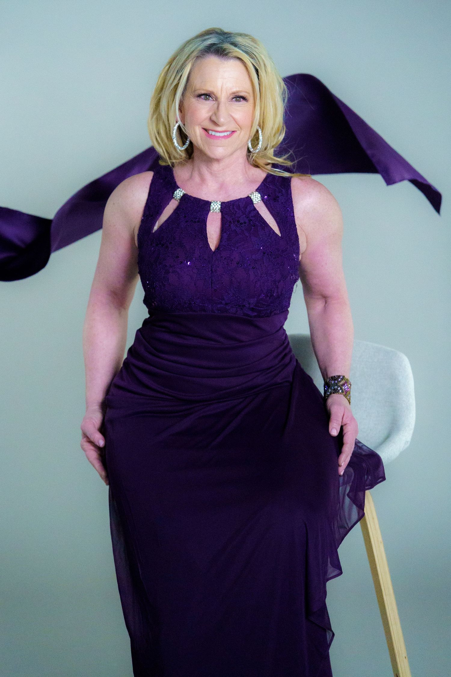 Person in an elegant deep purple evening gown with cutout details poses against a light background.
