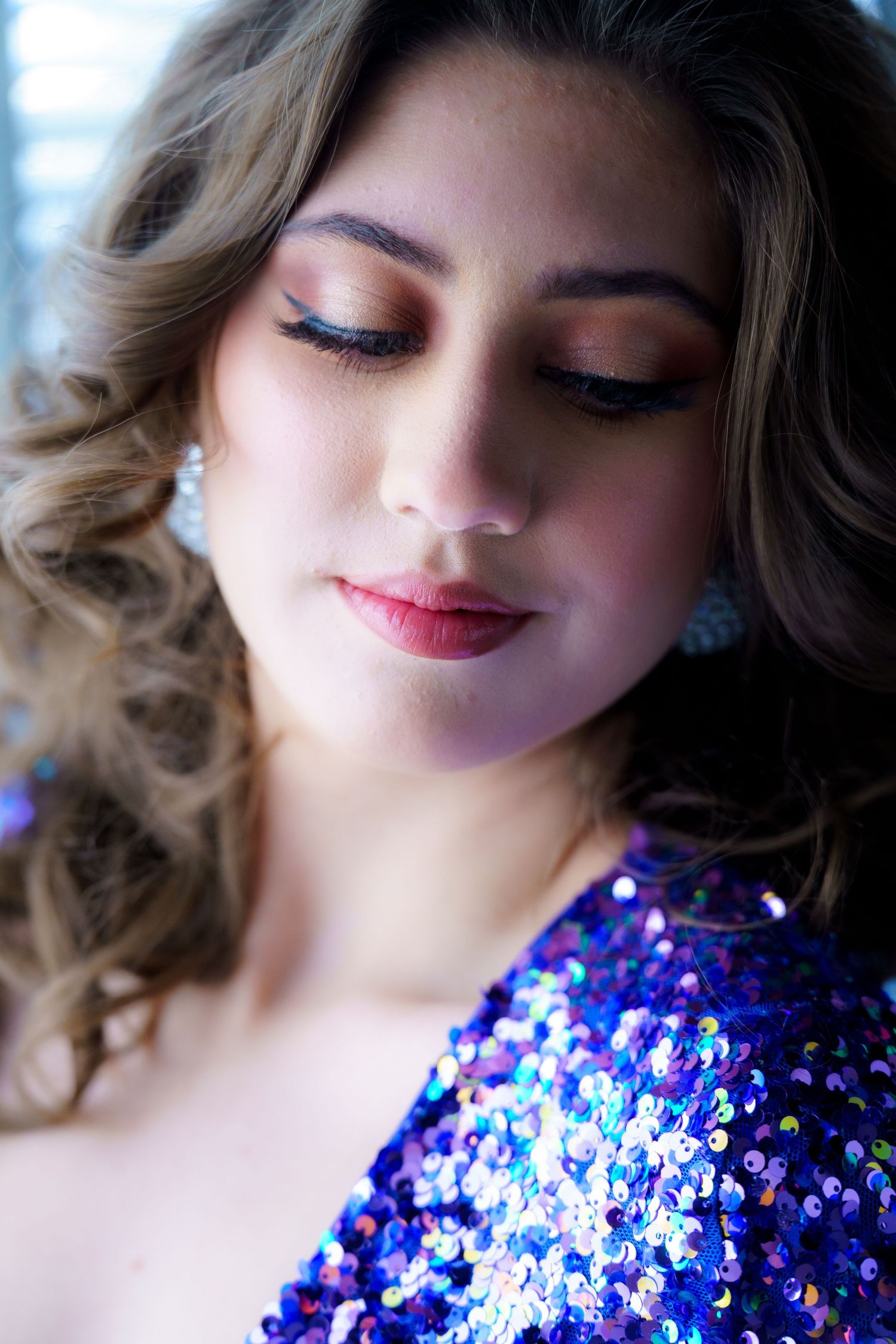 Close up beauty portrait with shimmering blue sequin dress, wavy hair, and glamorous evening makeup.