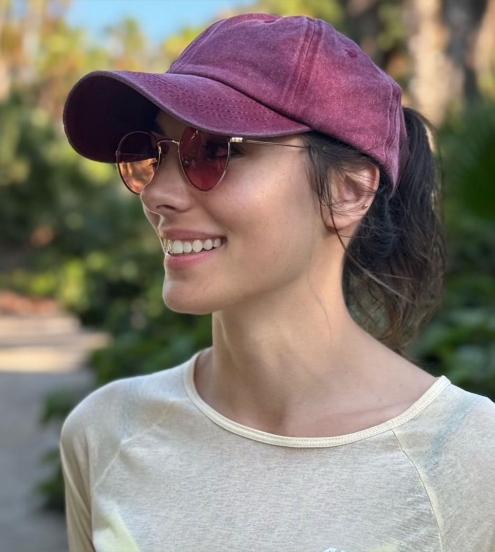 Kristen Lusk wearing a burgundy baseball cap and sunglasses smiles while enjoying a sunny day outdoors in Baja California, Mexico