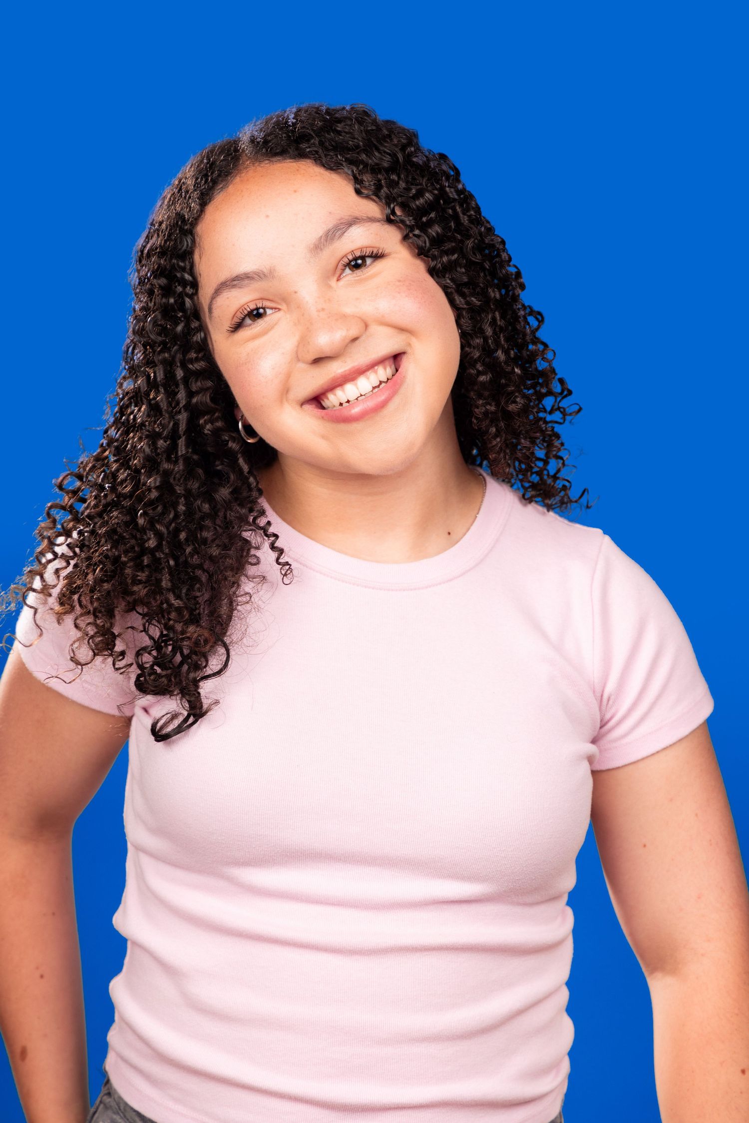 A series of four photos showing someone with curly dark hair wearing a pink t-shirt against a bright blue background.