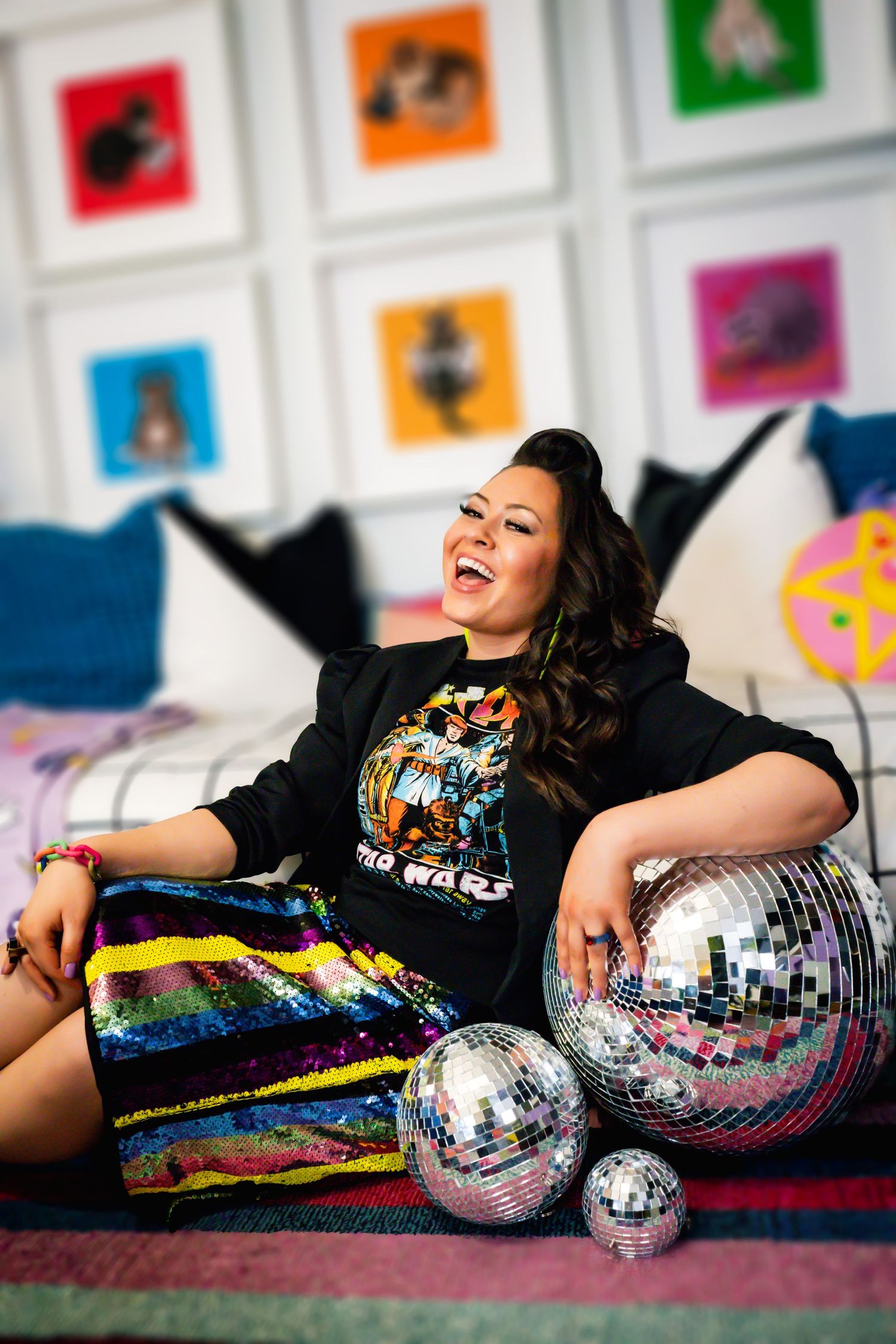 A person lounges on a couch wearing a Star Wars shirt and rainbow sequin skirt with disco balls as decor.