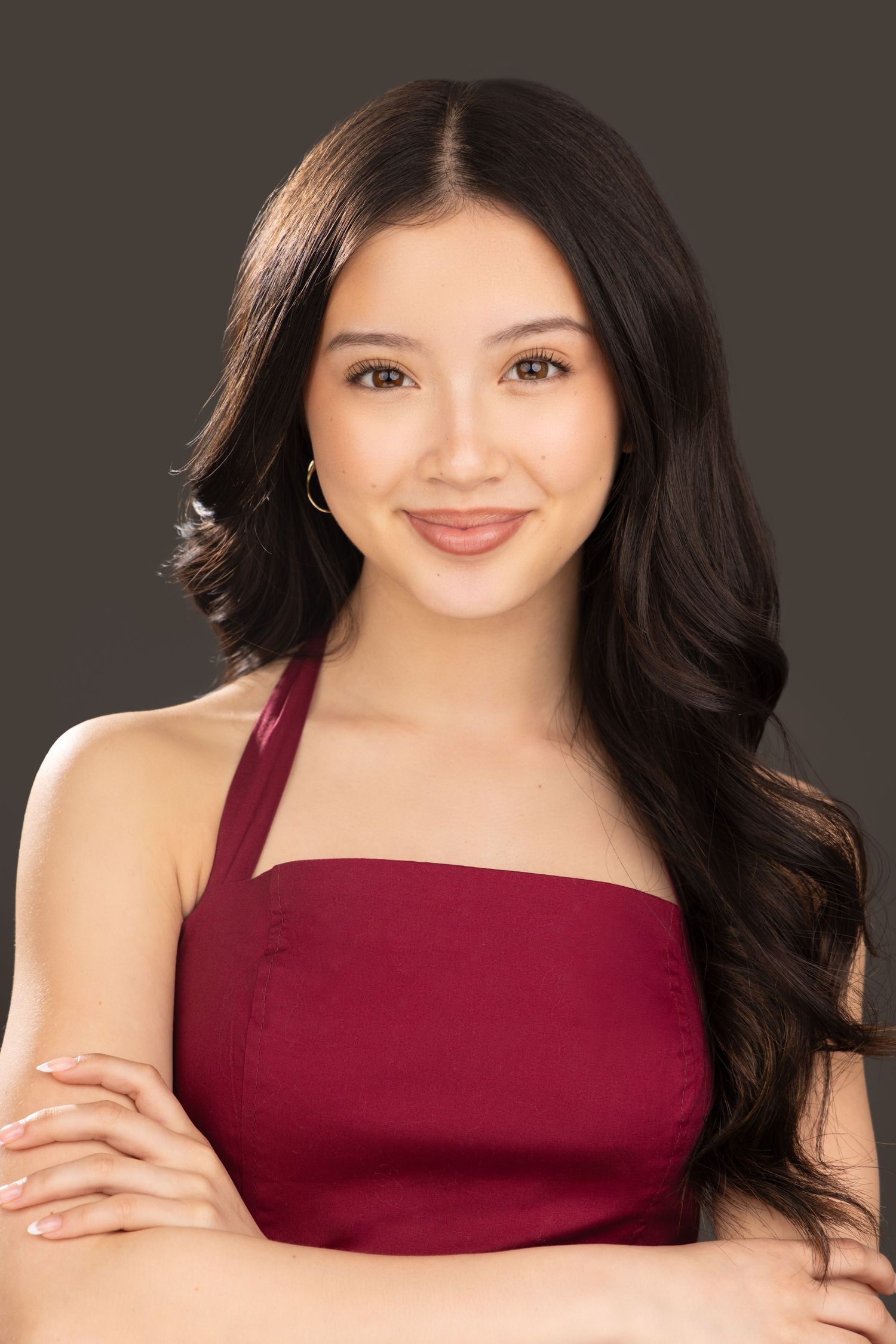 Professional portrait of someone with long dark hair wearing a burgundy halter top against a dark background.