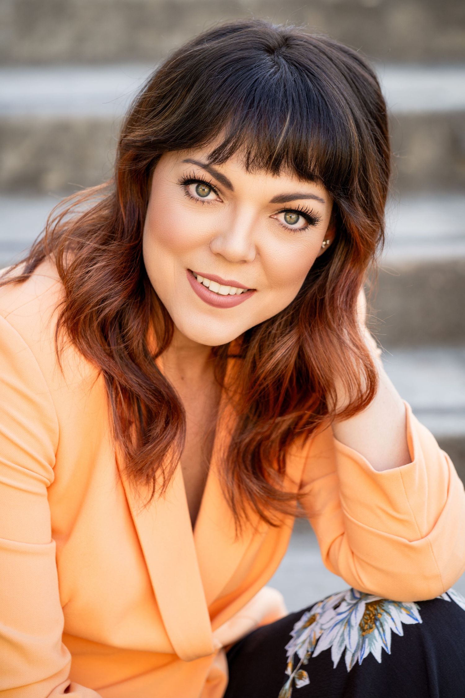 Portrait of someone in a peach-colored blazer smiling warmly at the camera against a blurred background.