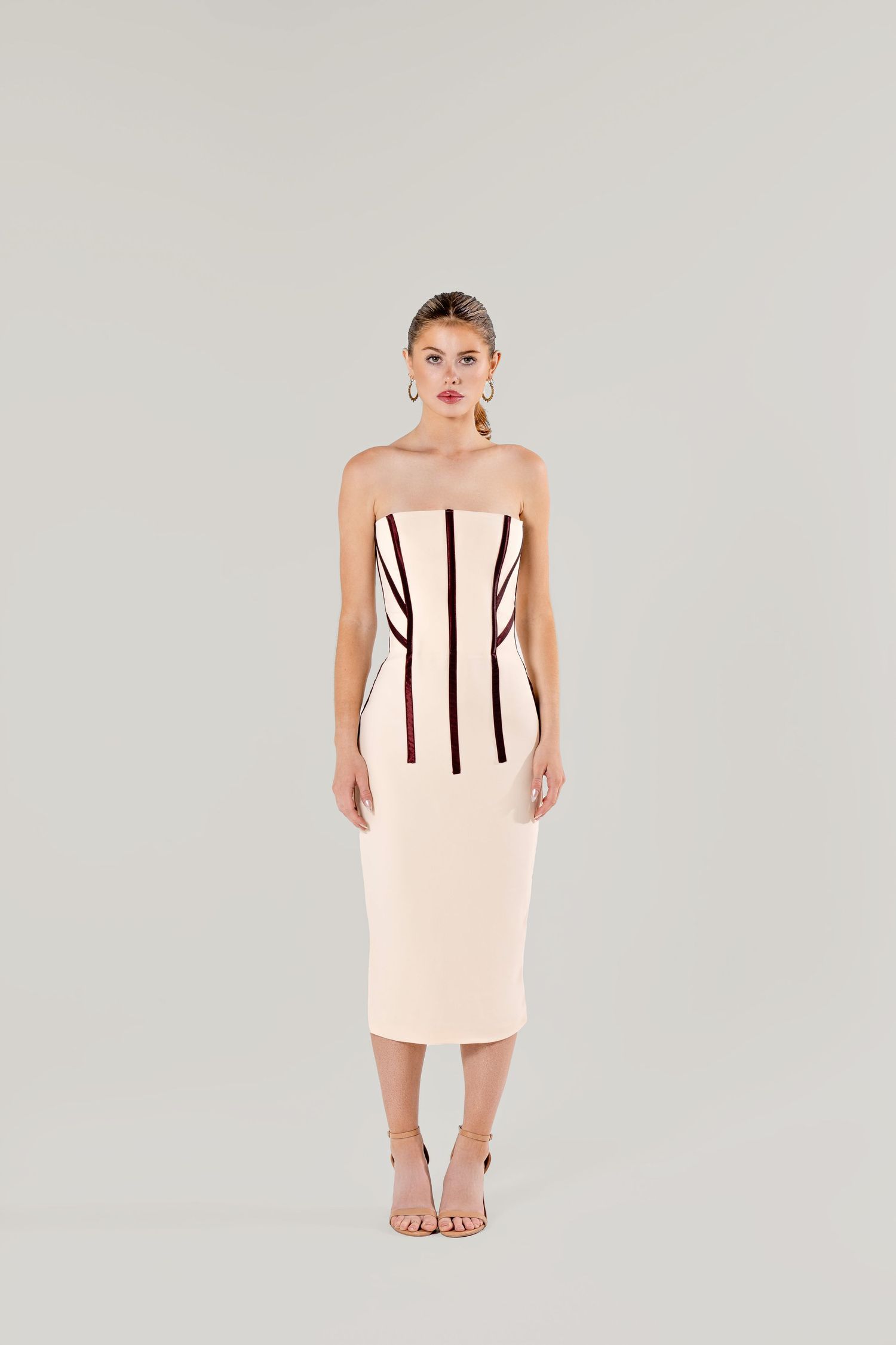 Elegant strapless bodycon dress in blush pink with vertical black stripes, worn barefoot against light gray background.