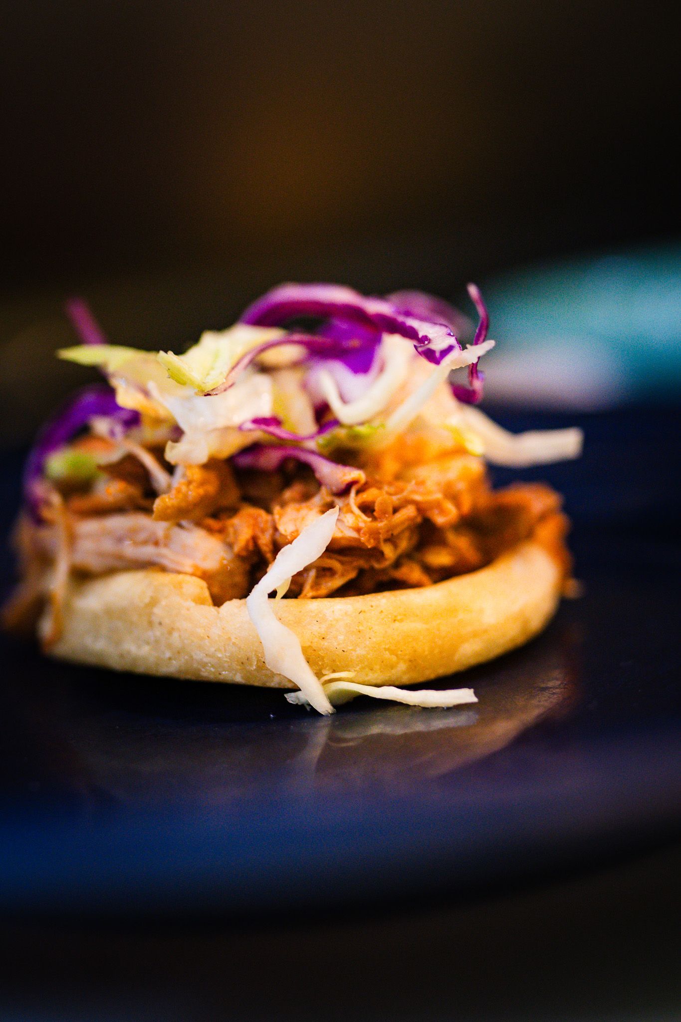 A gourmet pulled pork sandwich topped with vibrant purple cabbage slaw and served on a toasted brioche bun.