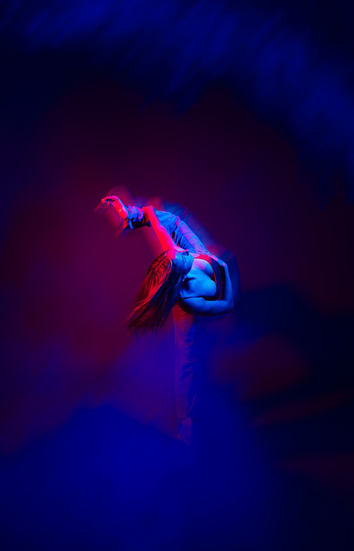 Dancer performing modern dance movement in dramatic red and blue lighting against dark background.