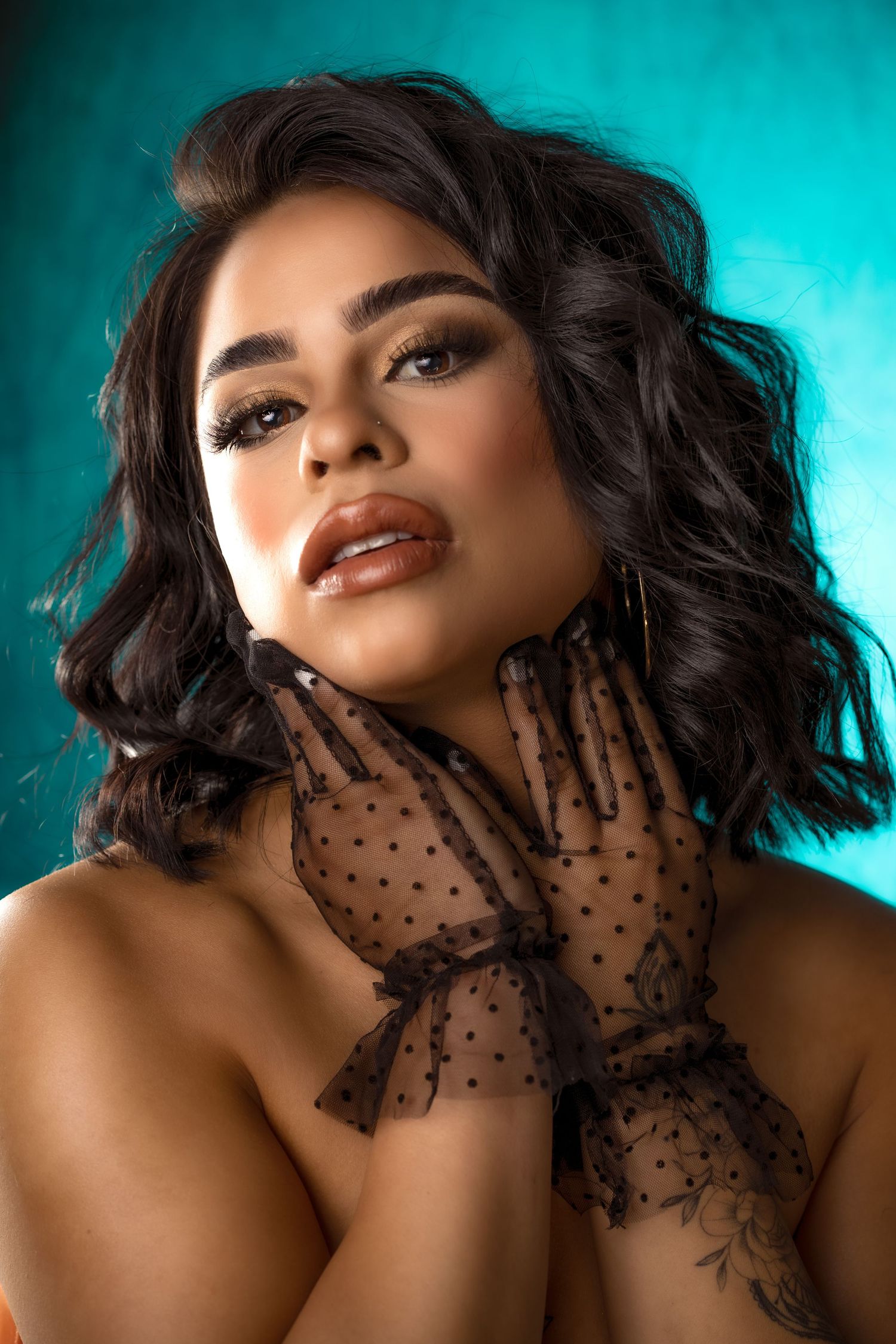 Portrait with black lace gloves and wavy hair against turquoise background in dramatic lighting and beauty styling.