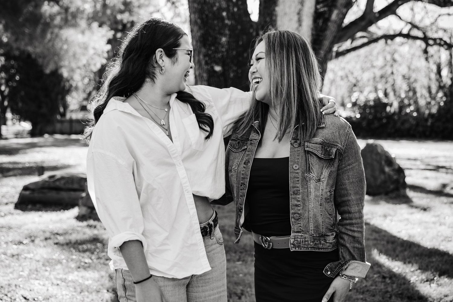 Black and white candid photo of two people sharing a joyful moment together outdoors in a park setting.